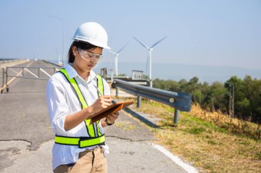 Asyalı kadın mühendisler dışarıdaki elektrik santralinin enerji türbinlerini kontrol edip teslim ediyorlar.