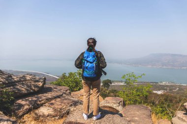 Özgürlük yolcusu kadın çantasıyla dağda duruyor ve güzel bir doğanın tadını çıkarıyor.