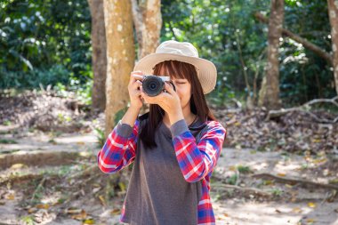 Ormanda elinde bir çanta ve kamerayla duran bir kadın turist.
