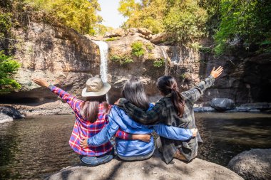 Özgürlük yolcusu bir grup kadın taşın üzerinde şelalede oturuyor ve güzel bir doğanın tadını çıkararak kollarını kaldırıyor. Seyahat kavramı