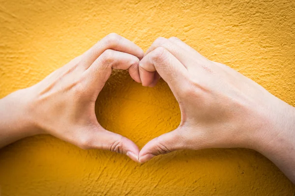 Woman holds heart shape on yellow wall — Stock Photo, Image