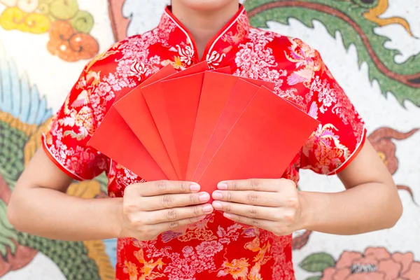 Feliz ano novo chinês, mulher asiática vestido tradicional cheongsam e qipao segurando envelopes vermelhos ang pow ou pacote vermelho cartão de presente monetário no padrão chinês fundo tradicional — Fotografia de Stock