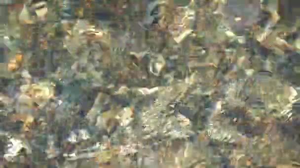 A textura do fundo. Muitas pedras pequenas são visíveis sob a água limpa. Ondas de água do mar, raios de sol nas rochas. — Vídeo de Stock