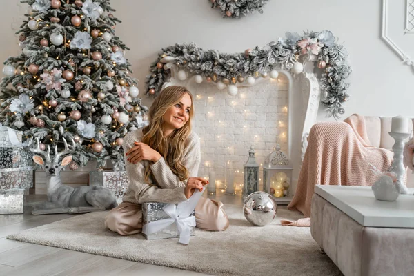 Feliz belleza rubia disfruta de la Navidad bajo el árbol de Navidad en una acogedora casa —  Fotos de Stock