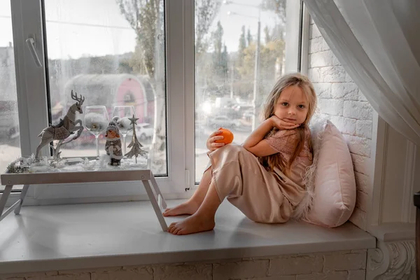 Отдыхающая и думающая девушка в пижаме сидит дома на подоконнике. Вид сбоку. — стоковое фото