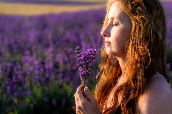 Mulher bonita está no campo da lavanda, detém um buquê de flores e gosta de aromaterapia. Os olhos das raparigas estão fechados. O conceito de aromaterapia, óleo de lavanda, sessão de fotos em lavanda — Fotografia de Stock