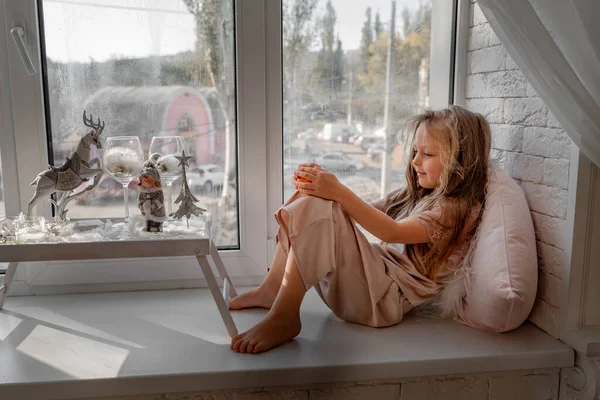 Niña descansando y pensando en pijamas sentada en el alféizar de la ventana en casa. Vista lateral. — Foto de Stock