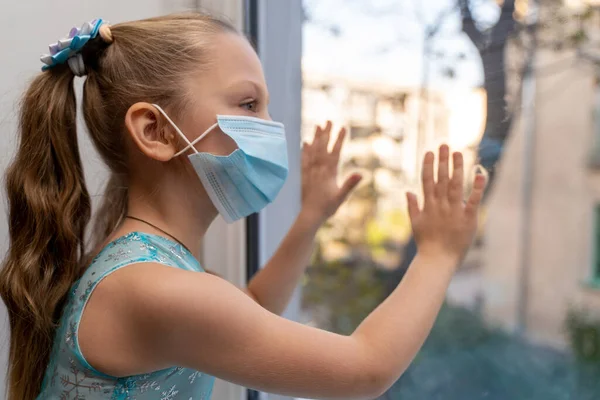 Máscara higiénica niña permanecer aislamiento en el hogar para la auto cuarentena para proteger contra el virus COVID-19y la contaminación del aire. Niñas miran por la ventana desde el dormitorio en casa — Foto de Stock