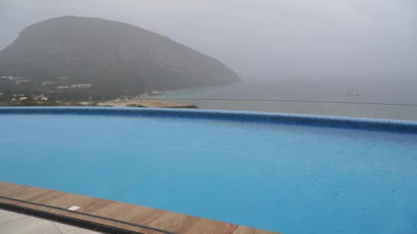 La pluie d'automne tombe en grosses gouttes sur la piscine extérieure chauffée. Piscine dans l'hôtel sur le fond de la montagne et de la mer. — Video