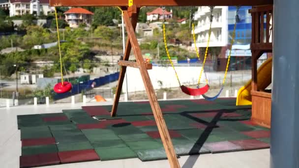 Leerer Spielplatz im Hintergrund der Stadt. Die Schaukel an den Ketten schwingt im Wind. Das Konzept der Epidemie ist alle zu Hause — Stockvideo