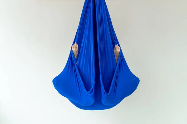 Work out on a hammock with a great yoga coach in the studio. Fly yoga. A girl sits in a lotus position in a blue anti-gravity yoga hammock