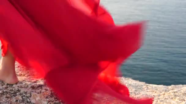 Close-up shot van de scharlaken zoom van de jurk, die fladdert in de wind, een vrouw die op blote voeten op een rots staat, tegen de achtergrond van de zee. — Stockvideo