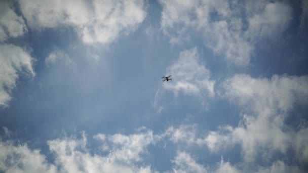 Dron leci na tle błękitnego nieba i chmur, widok z dołu. Czworokąt z kamerą unosi się na małej wysokości. Śruby napędowe dronów o szybkim obrocie. — Wideo stockowe