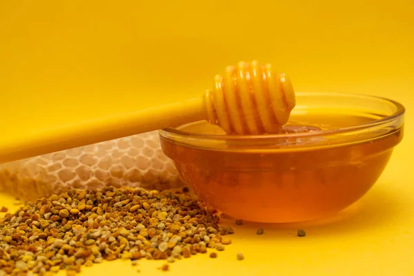 Eine Schöpfkelle Honig auf dem Hintergrund einer Bienenwabe. Honig-Leckerbissen in einem Glas Honiglöffel, Bienenbrot und eine Wabe aus Wachs auf gelbem Hintergrund. Konzept für gesunde Ernährung. — Stockfoto
