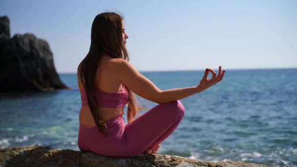Una giovane donna in abbigliamento sportivo si rilassa mentre pratica yoga sulla spiaggia vicino al mare calmo, primo piano delle mani, mudra gyan e loto posa. — Video Stock