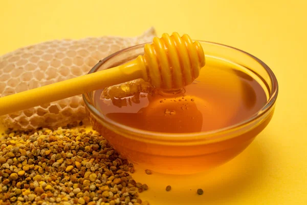 Eine Schöpfkelle Honig auf dem Hintergrund einer Bienenwabe. Honig-Leckerbissen in einem Glas Honiglöffel, Bienenbrot und eine Wabe aus Wachs auf gelbem Hintergrund. Konzept für gesunde Ernährung. — Stockfoto