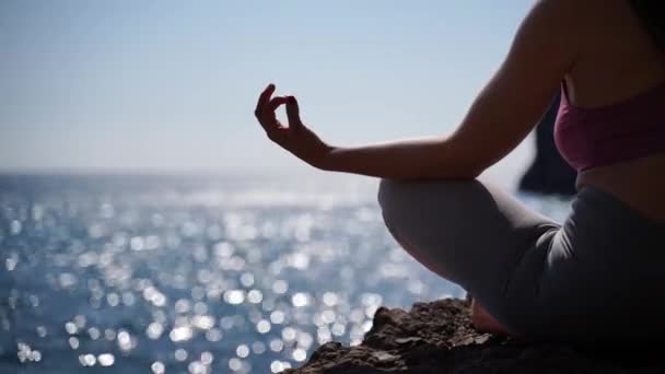 Una giovane donna in abbigliamento sportivo si rilassa mentre pratica yoga sulla spiaggia vicino al mare calmo, primo piano delle mani, mudra gyan e loto posa. — Video Stock