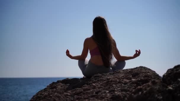 Una giovane donna in abbigliamento sportivo si rilassa mentre pratica yoga sulla spiaggia vicino al mare calmo, primo piano delle mani, mudra gyan e loto posa. — Video Stock