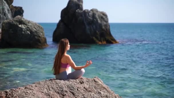 Una giovane donna in abbigliamento sportivo si rilassa mentre pratica yoga sulla spiaggia vicino al mare calmo, primo piano delle mani, mudra gyan e loto posa. — Video Stock