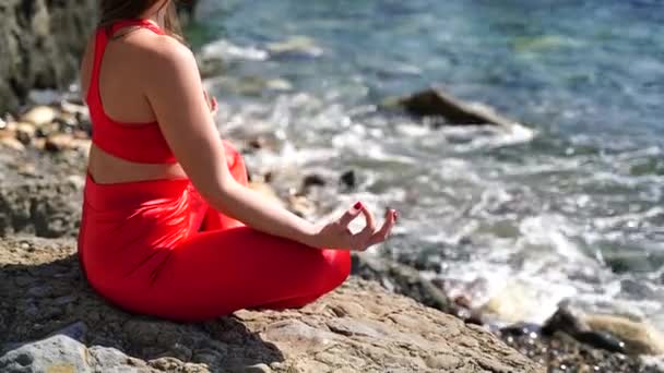 Una giovane donna in abbigliamento sportivo rosso si rilassa mentre pratica yoga sulla spiaggia in riva al mare calmo, primo piano delle mani, mudra gyan e loto posa. — Video Stock