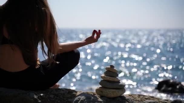 Eine junge Frau in roter Sportbekleidung entspannt sich, während sie am Strand am ruhigen Meer Yoga praktiziert, Hände in Großaufnahme, Gyan Mudra und Lotus-Pose. — Stockvideo