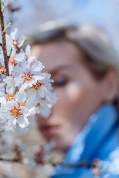 Retrato de una joven rubia en un floreciente jardín de primavera. Los almendros están floreciendo. La mujer está vestida con ropa azul.. —  Fotos de Stock