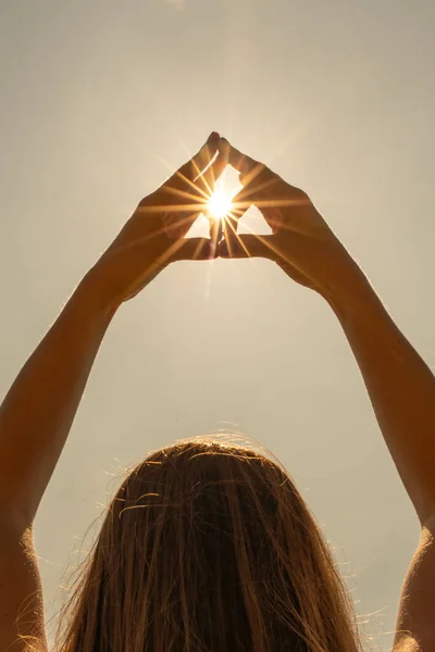 Ženské ruce v podobě srdce proti obloze míjejí sluneční paprsky. Ruce ve tvaru milostného srdce — Stock fotografie