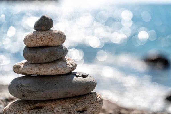 Tower of stones. Balanced pebble pyramid on the beach on a sunny day. Blue sea on the background. Selective focus, bokeh. Zen stones on the sea beach, meditation, spa, harmony, tranquility, balance