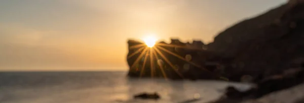 Banner. In blur An epic sunset on the sea - the sun sets behind the mountain and everything shines with warm light with long rays. — Stock Photo, Image