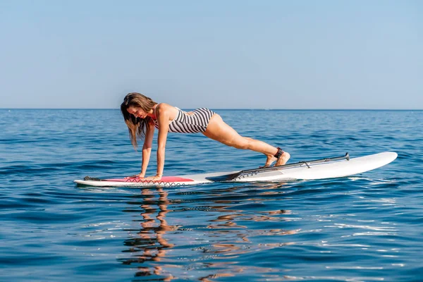 Sportief meisje op een kwade surfplank in zee op een zonnige zomerdag. In een gestreept zwempak is het in de bar. Zomer activiteiten bij Stortom by the sea — Stockfoto