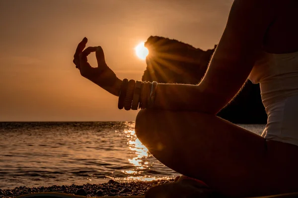 Jovem praticando ioga na praia com pôr do sol. Mantém os dedos ligados, o sol brilha através deles. O conceito de um estilo de vida saudável, harmonia. — Fotografia de Stock