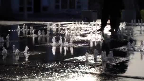 Vattenstrålar från stadens fontän i parken i solnedgången. Barn springer i fontänen. Vattentryck och tryck. Slänger vatten. Sakta i backarna. Närbild — Stockvideo