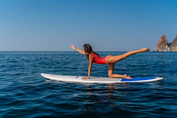 Chica deportiva en una tabla de surf en el mar en un día soleado de verano. Con un traje de baño rojo, se sienta en las hendiduras de la savia. Entretenimiento de verano en Stortom by the sea — Foto de Stock