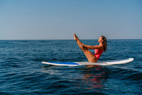 Menina desportiva em uma prancha de surf no mar em um dia ensolarado de verão. Em um maiô vermelho, ela se senta nas fendas na seiva. Entretenimento de verão no Stortom à beira-mar — Fotografia de Stock
