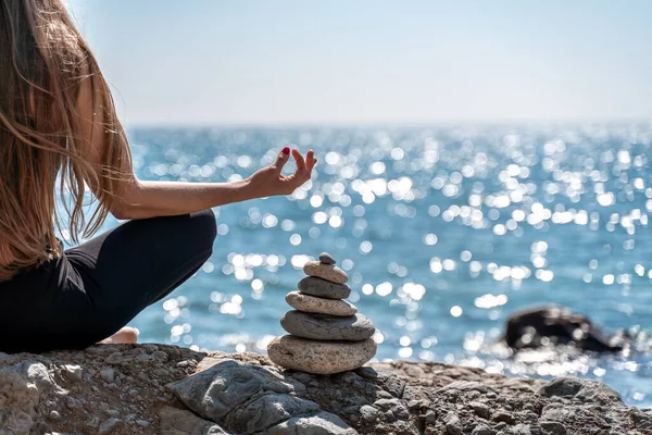 Ung kvinna i svart leggings och svart topp med långa flödande hår tränar sträcker sig utomhus vid havet på en solig dag. Kvinnors yoga, kondition, pilates. Begreppet en hälsosam livsstil, harmoni — Stockfoto