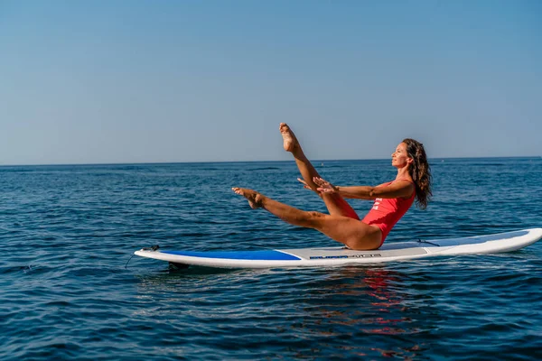 Σπορ κορίτσι σε σανίδα του σερφ στη θάλασσα μια ηλιόλουστη καλοκαιρινή μέρα. Με κόκκινο μαγιό, κάθεται στις σχισμές στον χυμό. Καλοκαιρινή διασκέδαση στο Stortom δίπλα στη θάλασσα — Φωτογραφία Αρχείου