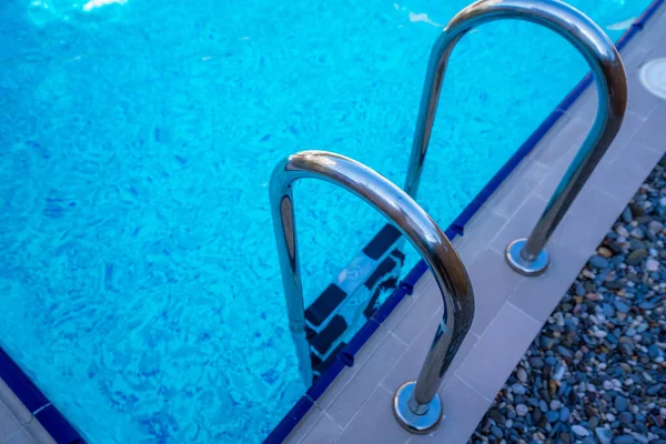 Background of blue transparent water in the swimming pool on the territory of the hotel. Descent to the pool with handrails. Rest and relaxation concept. Active rest by the sea