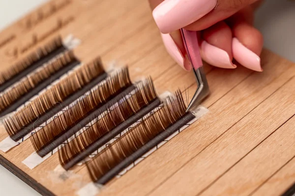 Eyelash extensions, lashmaker tools. Artificial eyelashes on a white tablet and pink silicone brush comb, close up.