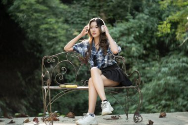 Güzel bir Asyalı genç kız kulaklıkla mutlu bir şekilde müzik dinliyor..