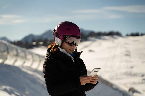 Young girl with a ski helmet consulting her mobile phone in a ski resort in the Alps