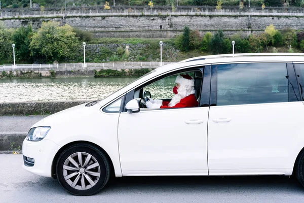 Santa Claus driving a car to deliver gifts to children with red face masks due to the covid19 coronavirus pandemic in Christmas 2020
