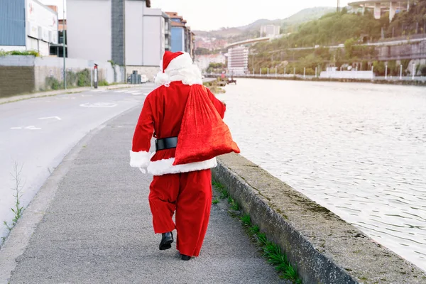 Back portrait of Santa Claus walking down the street with a sack full of presents to give to the children in the Christmas of 2020