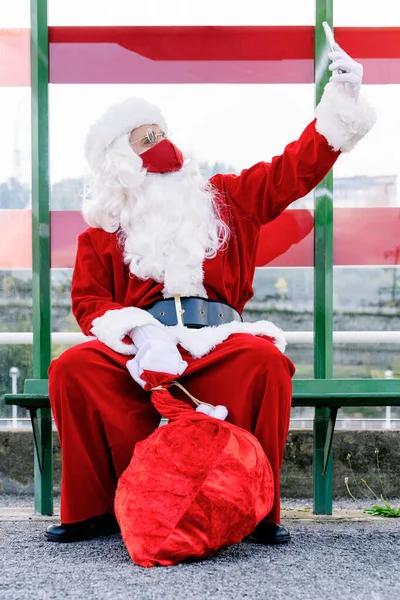Portret Wyprostowanego Świętego Mikołaja Siedzącego Przystanku Autobusowym Telefonem Komórkowym Robiącego — Zdjęcie stockowe