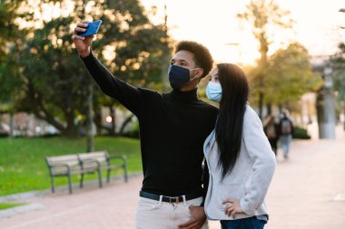 2020 yılında San Valentin 'de Coronavirus Covid-19 salgınından dolayı yüz maskesi takıp Bilbao' yu ziyaret ettikleri için cep telefonuyla selfie çeken genç bir erkek çocuğunun portresi.