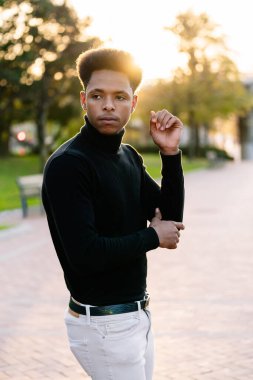 Güzel bir gün batımının güneşiyle caddede afro saçlı, poz veren ve şehir tarzı kıyafetlerle yürüyen yakışıklı bir Faslı 'nın şık portresi.