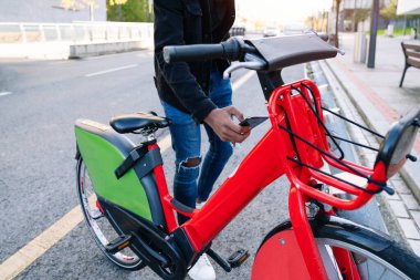Man 's Hand, caddedeki bisiklet parkından kiralık bir bisikleti almak için cep telefonunu kullanıyor.