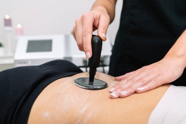 Short plane of Beautician giving radio frequency treatment to a woman in the stomach that outlines and stimulates healthy cell function, revitalization and cellulite removal