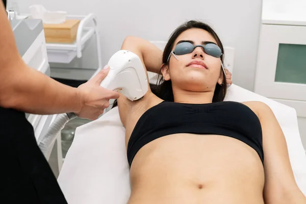 short shot Aesthetician giving laser diode treatment to a woman in the armpit where the client wears laser protection glasses