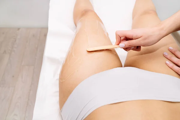 Short hand flat photograph of beautician giving waxing treatment to a woman on her thigh