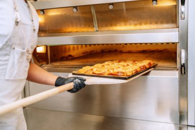 Fırıncı elinde bir tepsi hamur işi palmiye taşır ve fırının fırınına koyar.